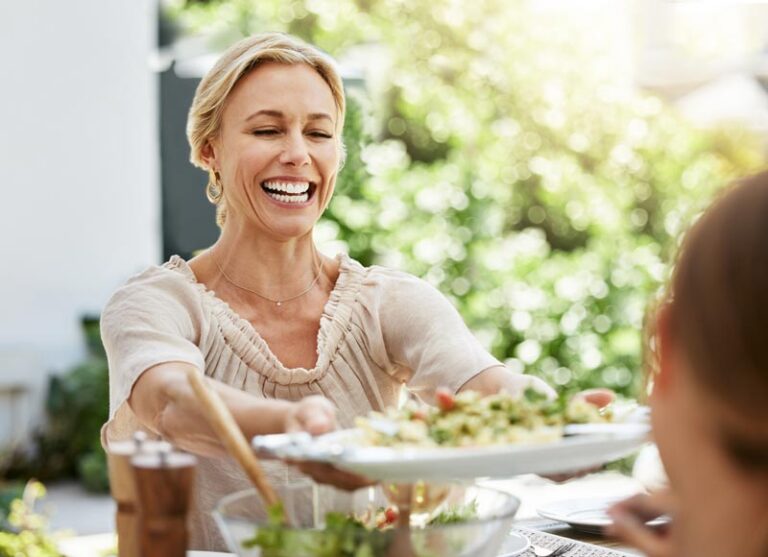 Smiling woman serving a healthy meal outdoors, emphasizing the importance of nutrition for gut health, aligned with Biohm Technologies' focus on bacterial and fungal communities in the gut.